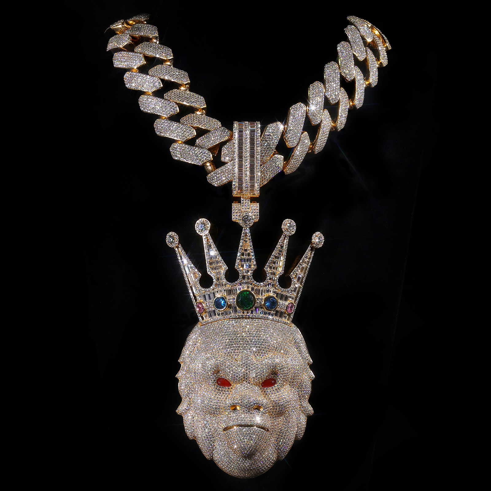 Crowned iced-out pendant with a gold-tone Cuban link chain on black